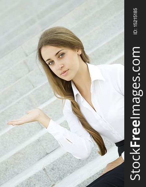 Businesswoman gesturing. Young business woman on a background of office building showing stairs. Businesswoman gesturing. Young business woman on a background of office building showing stairs