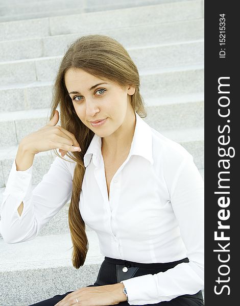 Young businesswoman outdoors on the stairs near the office building shows a sign of Call me