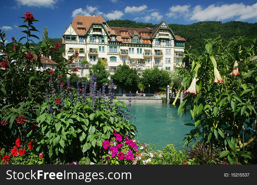 A Swiss chalet-type building, framed by flowers, is located across the Aare River in the old town of Thun, Switzerland.