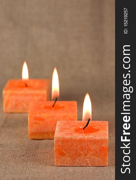 Three burning orange aromatic candles on the fabric background. Three burning orange aromatic candles on the fabric background