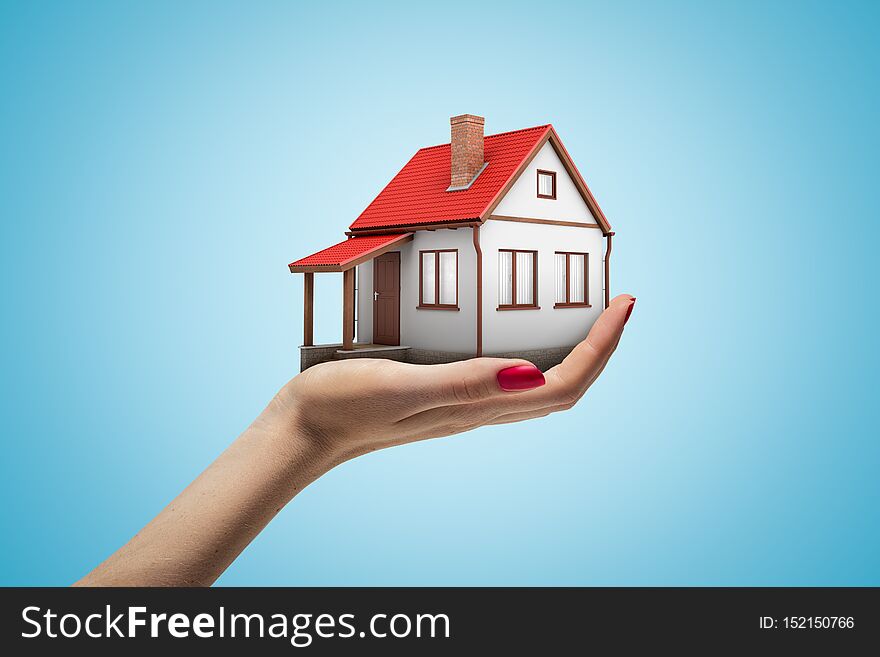 Side closeup of woman`s hand facing up and holding small one-storey house on light blue gradient background.