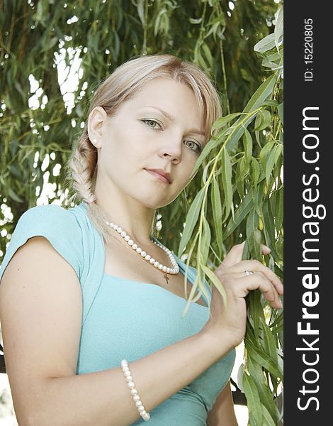 The girl with a plait in a beads among green branches of a willow. The girl with a plait in a beads among green branches of a willow