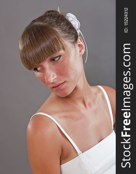 Sad woman in white dress posing on the grey background