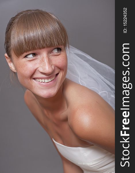 Laughing bride with veil on the grey background