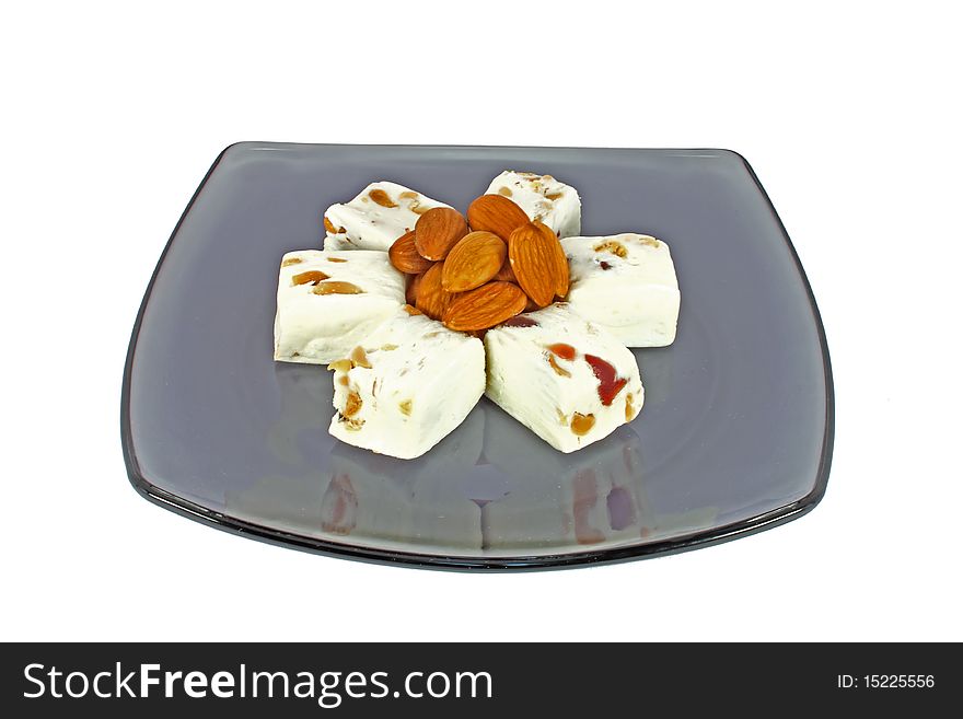 Delicious nougat with almonds on black glass plate, isolated on white