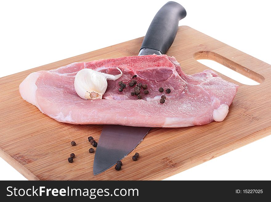 Piece of crude meat with black pepper and garlic on a kitchen board. Piece of crude meat with black pepper and garlic on a kitchen board.