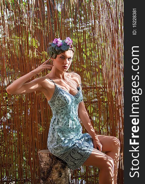 Beautiful girl with a wreath of flowers on her head on the background of bamboo fence