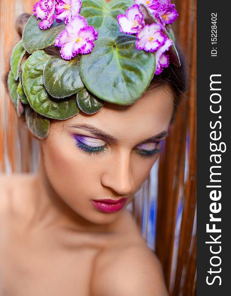 Beautiful girl with a wreath of flowers on her head on the background of bamboo fence