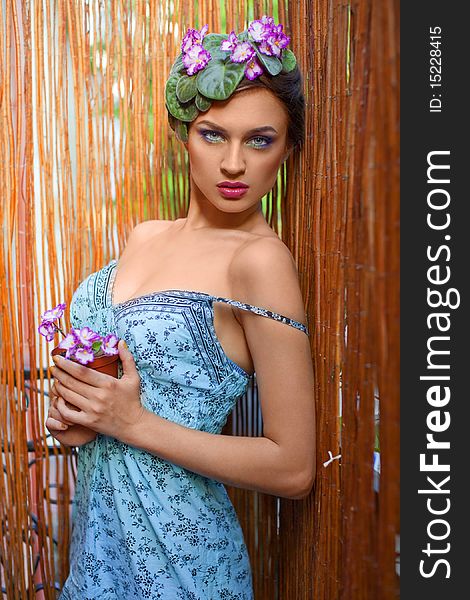 Beautiful girl with a wreath of flowers on her head on the background of bamboo fence