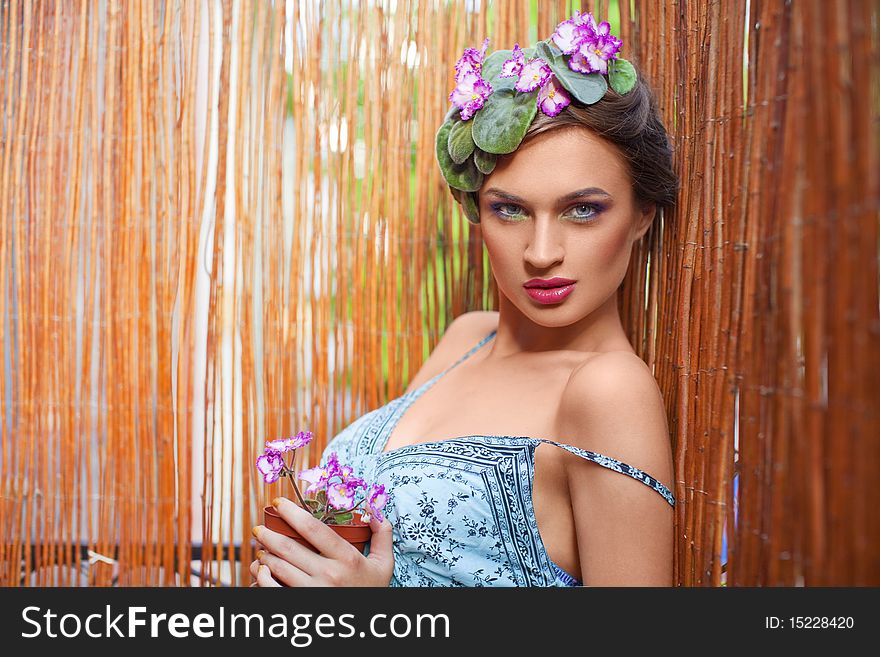 Beautiful girl with a wreath of flowers on her head on the background of bamboo fence