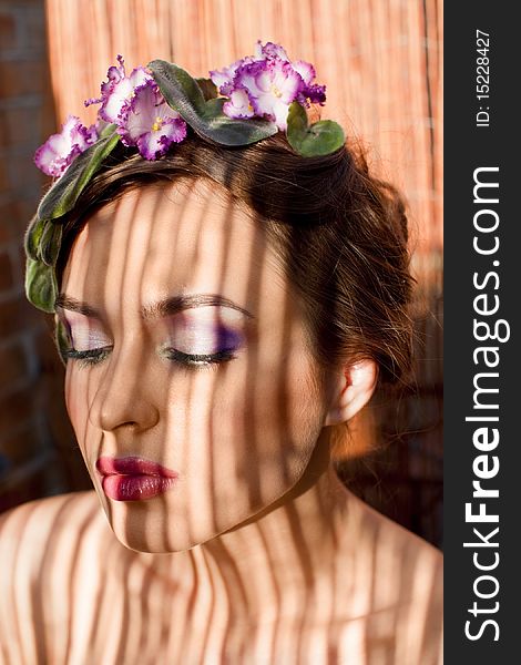 Beautiful girl with a wreath of flowers on her head on the background of bamboo fence