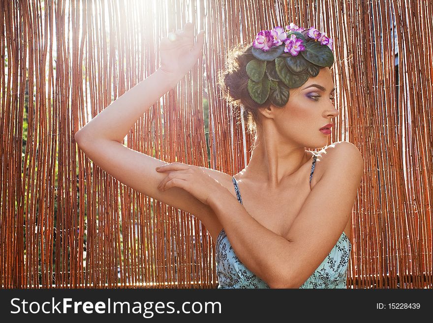 Beautiful girl with a wreath of flowers on her head on the background of bamboo fence