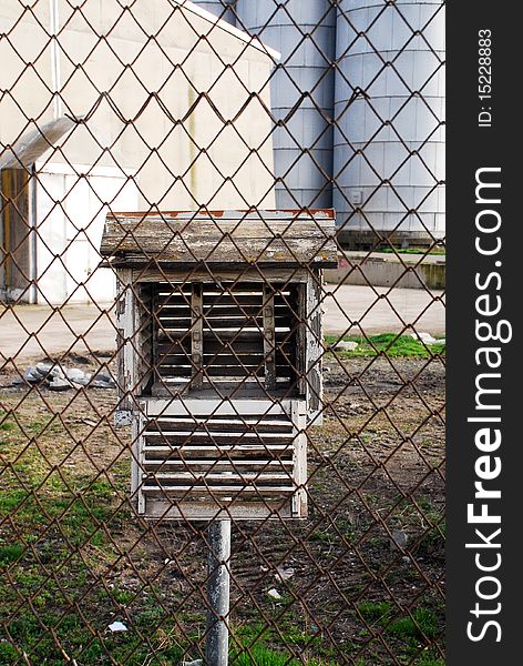 Decorative birdhouse made of tree and mounted on a piece of wood behind a chain link fence. Decorative birdhouse made of tree and mounted on a piece of wood behind a chain link fence.