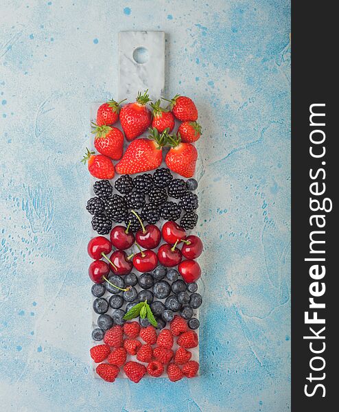Fresh organic summer berries mix on white marble board on blue kitchen table background. Raspberries, strawberries, blueberries