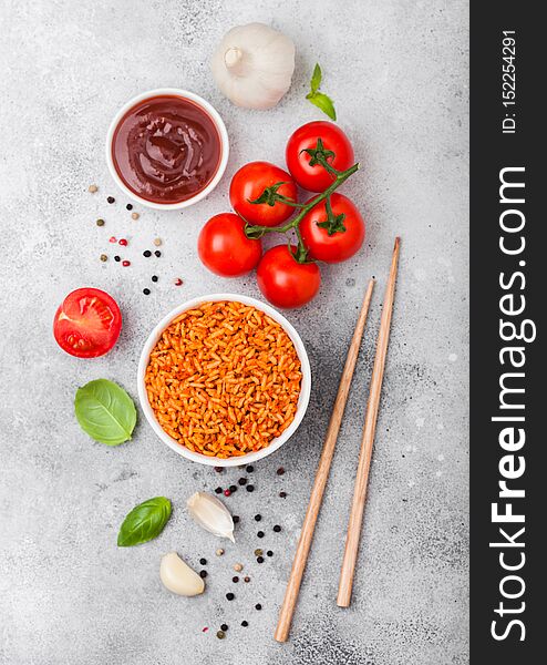 White plate bowl of rice with tomato and basil and garlic and chopsticks on light stone background. Top view
