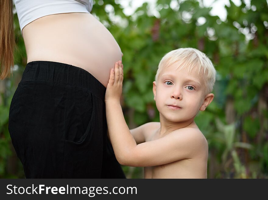 Little blond boy strokes the belly of his pregnant mother. Family concept