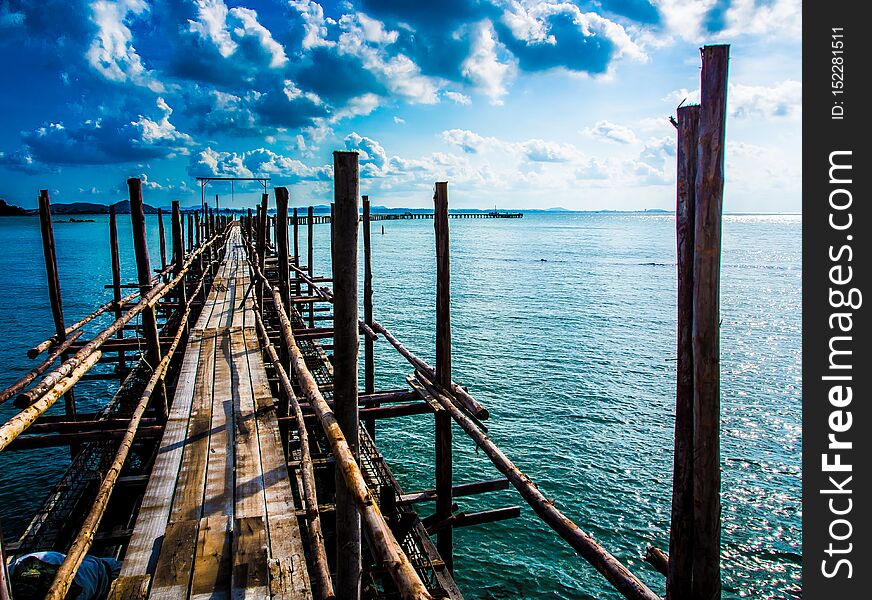 A wooden bridge with a path to the sea, the day when the sky is blue, the sky is bright, the blue sea is a wooden boat dock of olden days