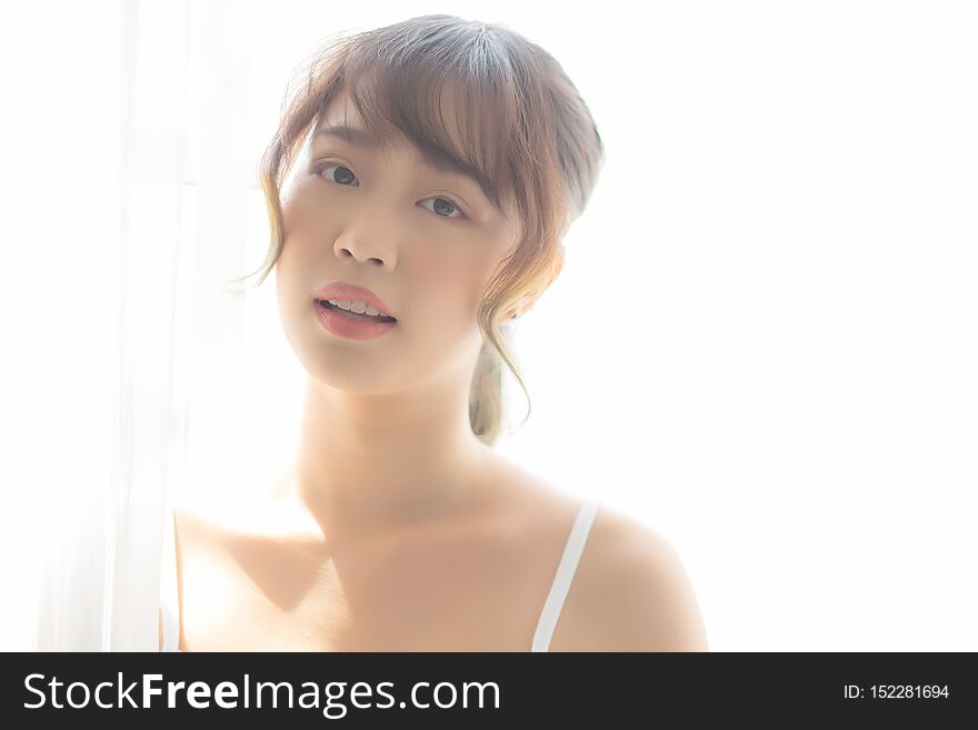 Portrait of beautiful young asian woman standing the window and smile while wake up with sunrise at morning