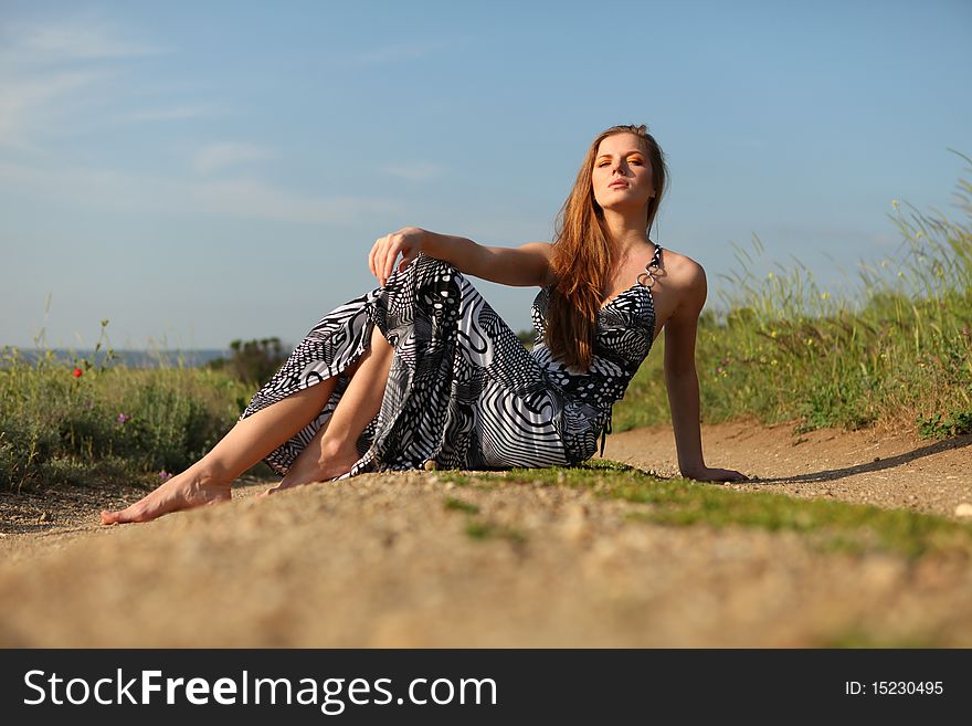 Young beautiful woman in dress sitting on the road. Young beautiful woman in dress sitting on the road