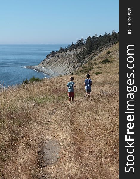 Boys hiking on a trail in tall grass, ocean in the foreground. Boys hiking on a trail in tall grass, ocean in the foreground.