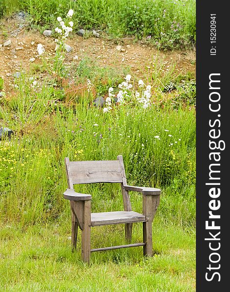 A wooden chair in front of a hill with grass and wild flowers.