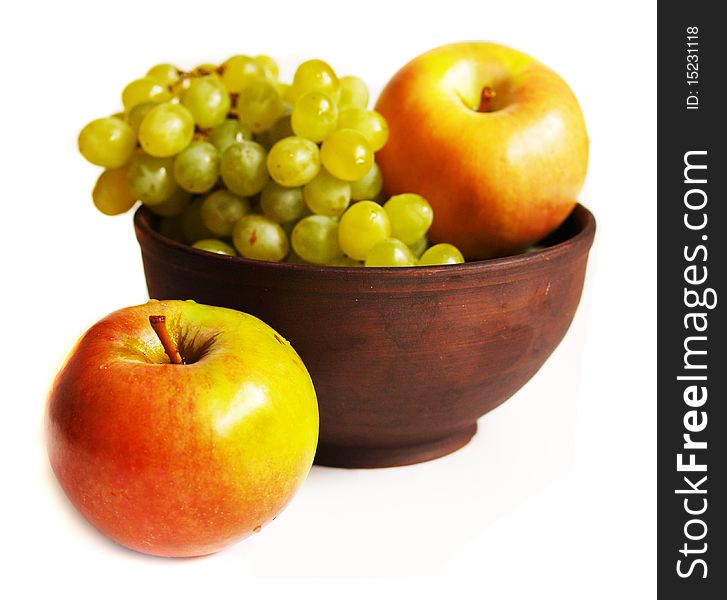 Juicy grapes and apples in the clay plate isolated on white background