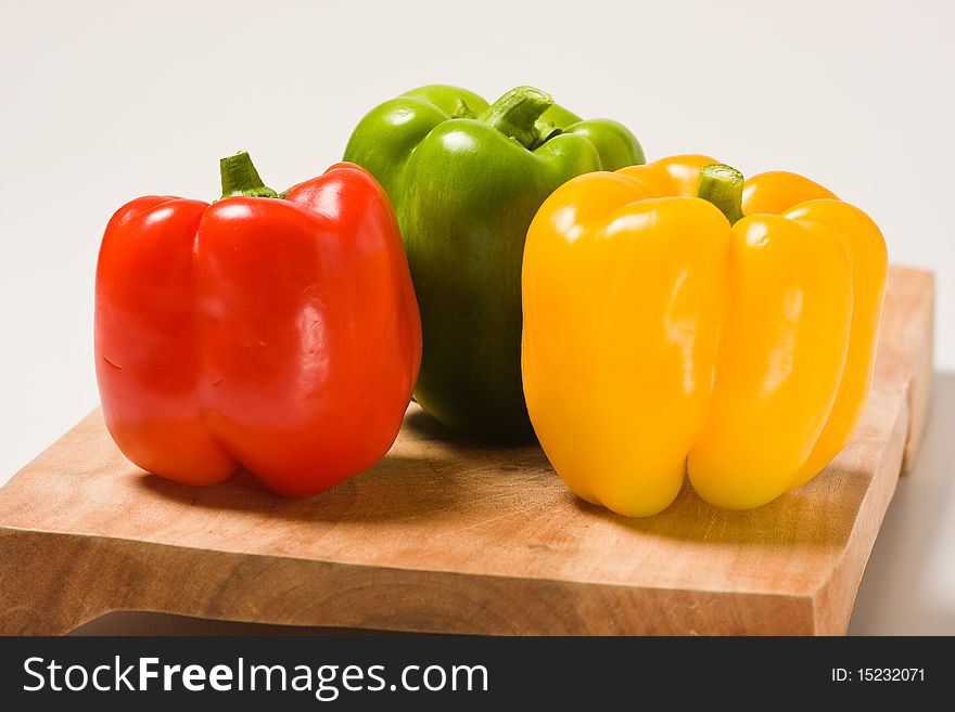 A red, green and yellow bell pepper sitting on a wooden cutting board. A red, green and yellow bell pepper sitting on a wooden cutting board