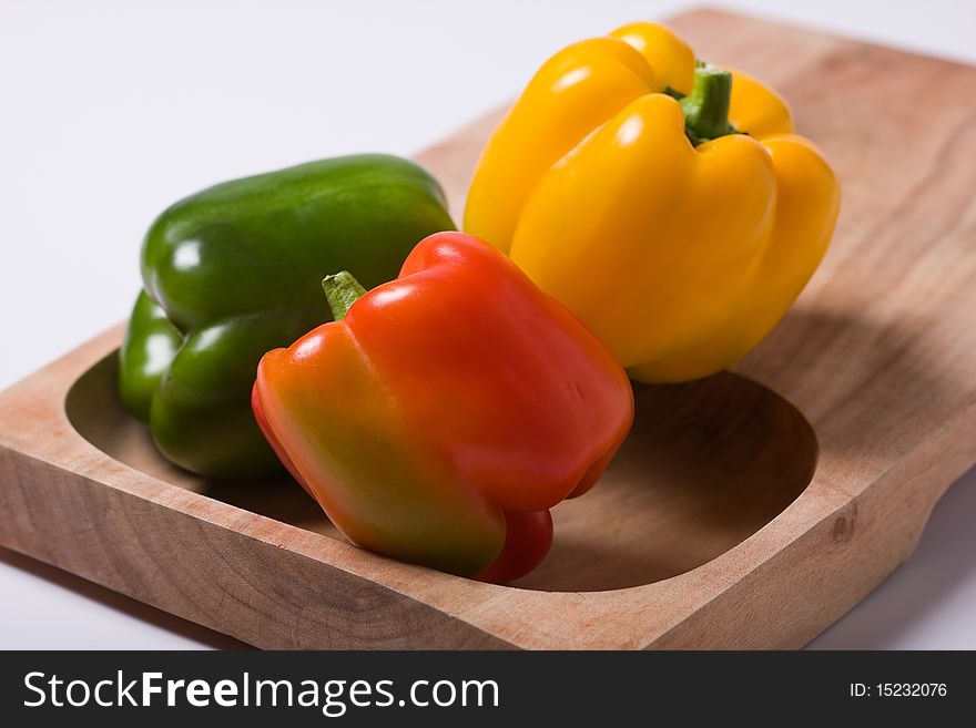 Green, red and yellow bell peppers sitting on a wooden cutting board