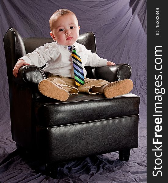 Baby wearing a colorful neck tie, bored expression sitting in a leather chair. Baby wearing a colorful neck tie, bored expression sitting in a leather chair