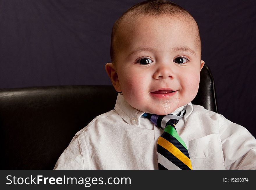 Baby wearing a colorful neck tie smiling laughing sitting in a leather chair. Baby wearing a colorful neck tie smiling laughing sitting in a leather chair
