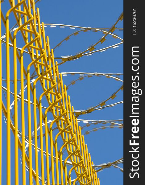 Bright yellow fence with barbed wire on a background of blue sky. Bright yellow fence with barbed wire on a background of blue sky