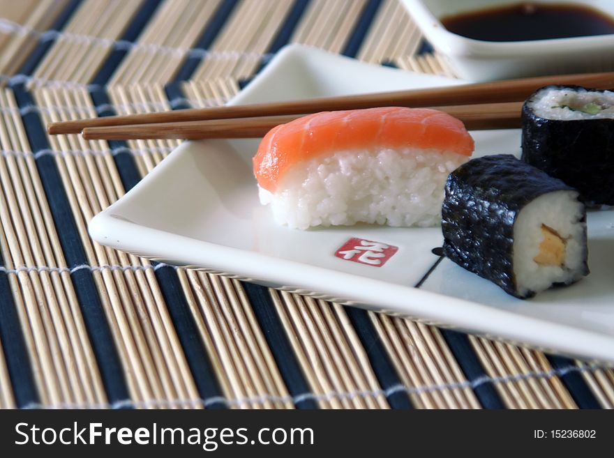 Small sushi on a plate with wood chopsticks on a rectangular decorated plate, on a wood table-cloth, close-up. Small sushi on a plate with wood chopsticks on a rectangular decorated plate, on a wood table-cloth, close-up