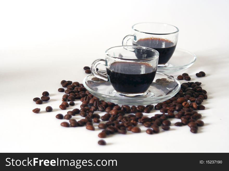 Two transparent glass coffee cups and some coffee beans on white background