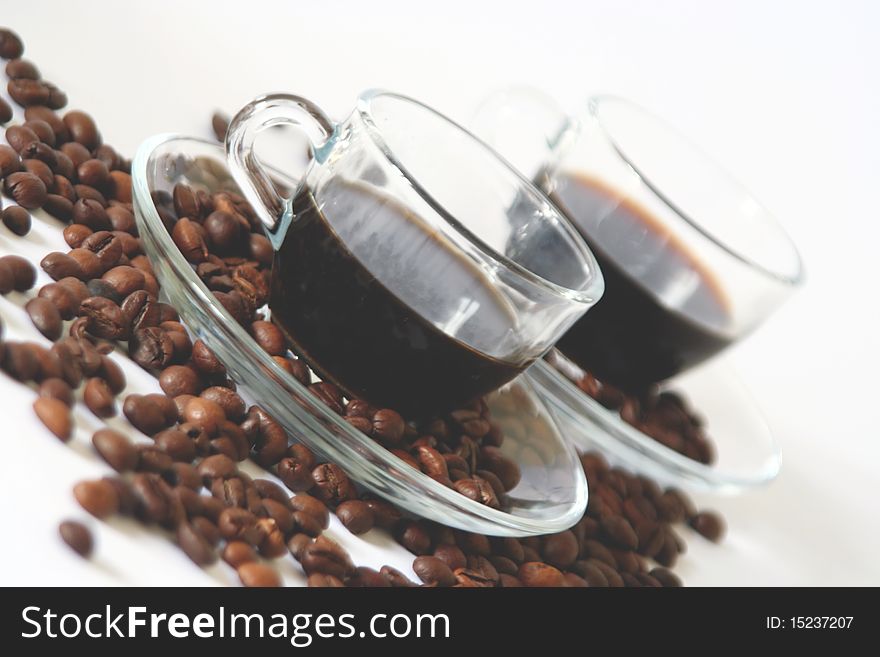 Two transparent glass coffee cups and some coffee beans on white background in diagonal. Two transparent glass coffee cups and some coffee beans on white background in diagonal