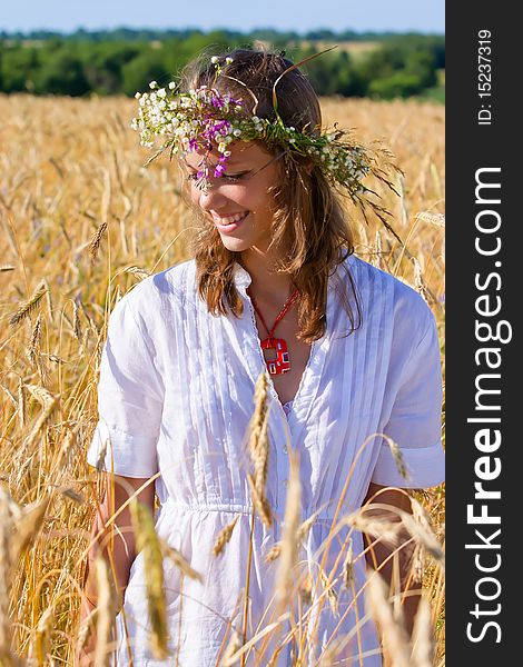 Russian girl in a wreath from camomiles is in a wheaten field