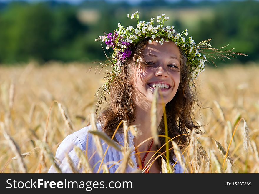 Russian girl in a wreath from camomiles is in a wheaten field