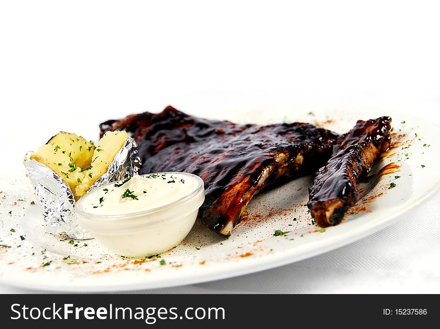 Pork ribs with a baked potato and sour cream on a white ceramic plate garnished with parsley