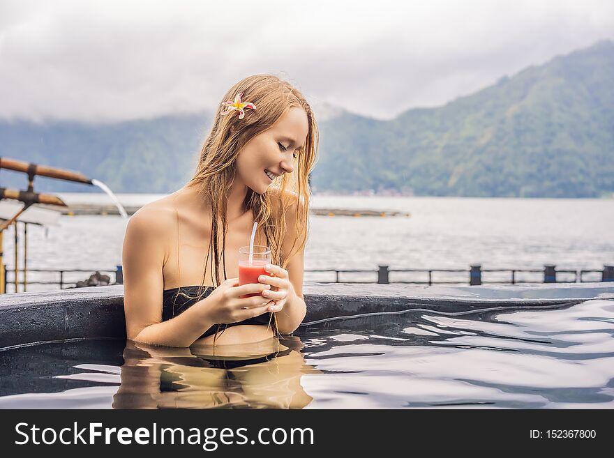 Geothermal spa. Woman relaxing in hot spring pool against the lake. hot springs concept. Drinking guava juice