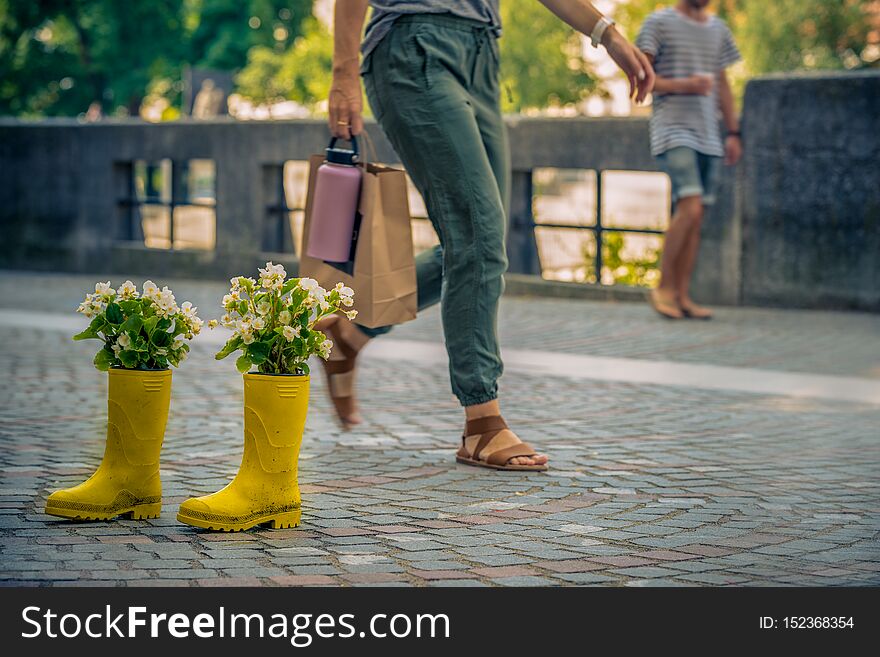 A pair of yellow rubber boots in the middle of a street in which flowers grow