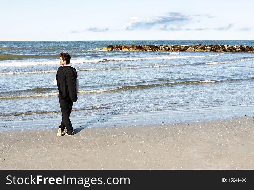 Horizontal photo of businessman looking at ocean barefoot in suit and holding jacket, blue sky and ocean in background. Horizontal photo of businessman looking at ocean barefoot in suit and holding jacket, blue sky and ocean in background