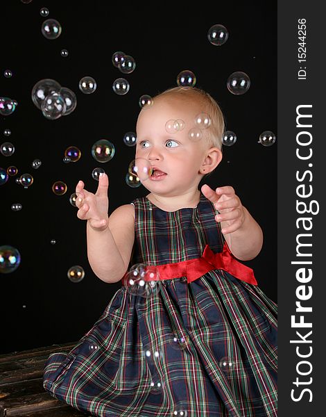 Cute blond toddler girl surrounded by bubbles sitting on a wooden trunk. Cute blond toddler girl surrounded by bubbles sitting on a wooden trunk
