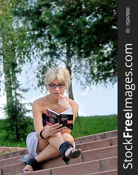 Charming young woman read book in urban park summer day