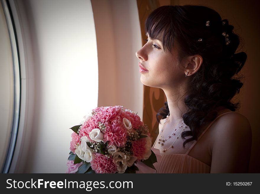 The bride looks out the window and holds a bouquet of flowers. The bride looks out the window and holds a bouquet of flowers