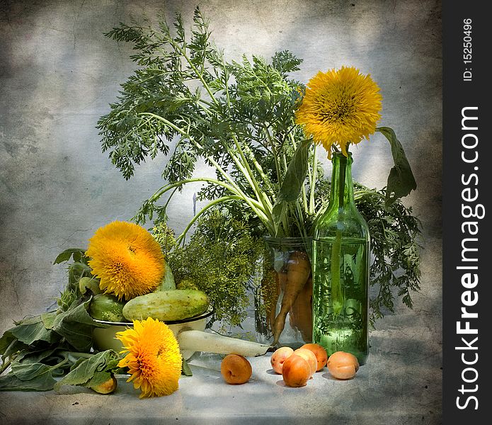 One sunflower stands in a bottle, other two lie on a table, alongside there are cucumbers and carrot in a glass jar. One sunflower stands in a bottle, other two lie on a table, alongside there are cucumbers and carrot in a glass jar.