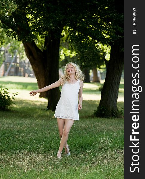 Young blond is dancing in her sundress under shadily trees in the park