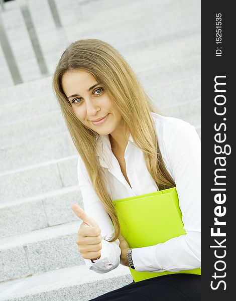 Attractive young businesswoman smiling with a green folder on the chest. Sign OK. Attractive young businesswoman smiling with a green folder on the chest. Sign OK