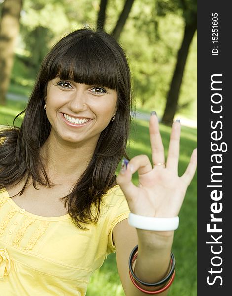 Young beautiful woman is smiling in a park and shows the sign OK