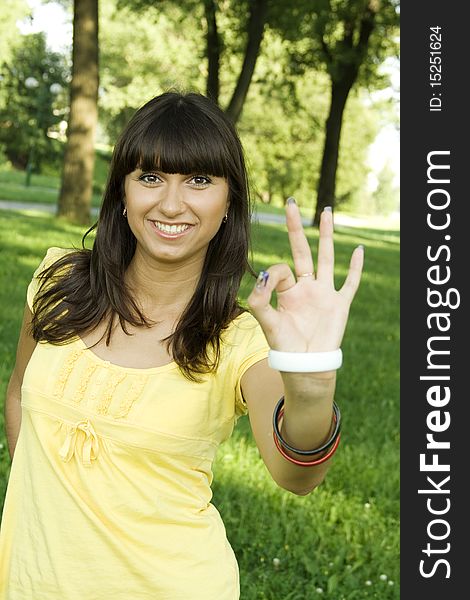 Young beautiful woman is smiling in a park and shows the sign OK