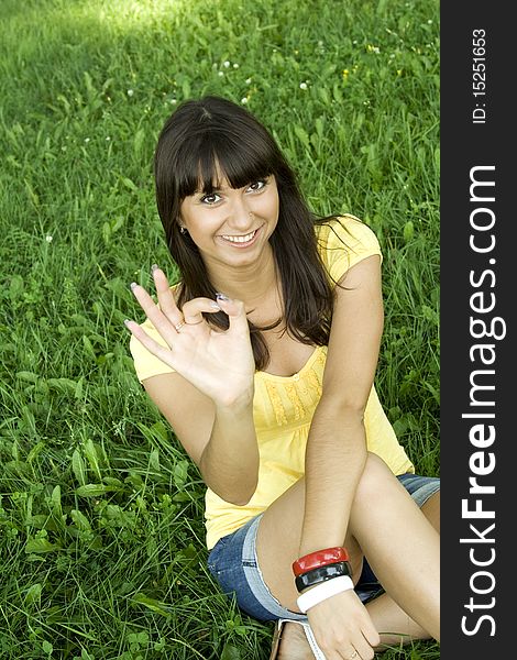 Young beautiful woman sitting on the grass in park smiling and showing signs OK. Young beautiful woman sitting on the grass in park smiling and showing signs OK