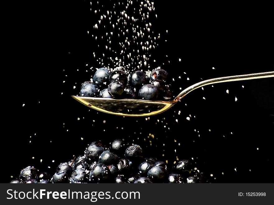 Spoon with huckleberry with pouring sugar on black background. Spoon with huckleberry with pouring sugar on black background